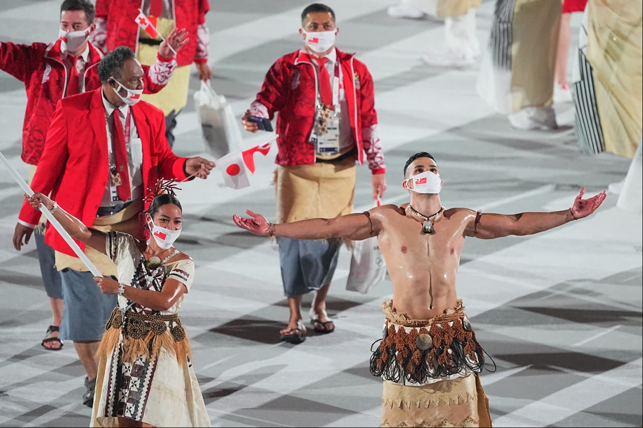 El nativo de Tonga con su torso desnudo pero esta vez enmascarado por el coronavirus. Parte de las fuertes medidas para evitar la propagación del covid-19 en Tokio.
<br>
<br>El taekwondista explicó en 2016 que el atuendo y el aceite que usó en el desfile era su forma de honrar a su cultura de Oceanía. Tonga es un pequeño país en el Pacífico formado por un grupo de islas donde viven unos 100,000 habitantes. 
<br>