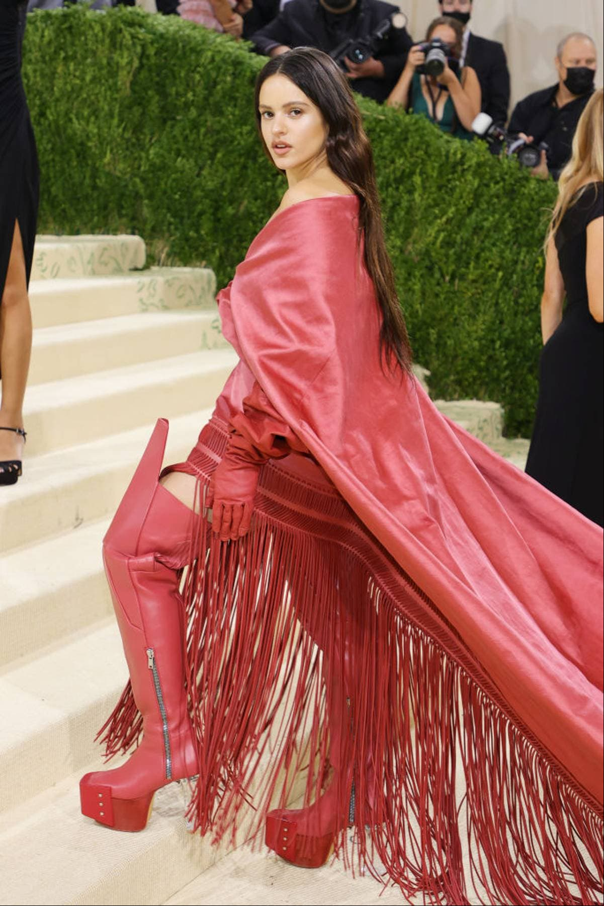 Rosalía apareció en la MET Gala con un vestido de Rick Owens. El atuendo impresionó por el guiño que hizo a España, pues está inspirado en un mantón de Manila. Este espectacular look está conformado por un pantalón corto de tiro alto, botas altas y guantes largos.