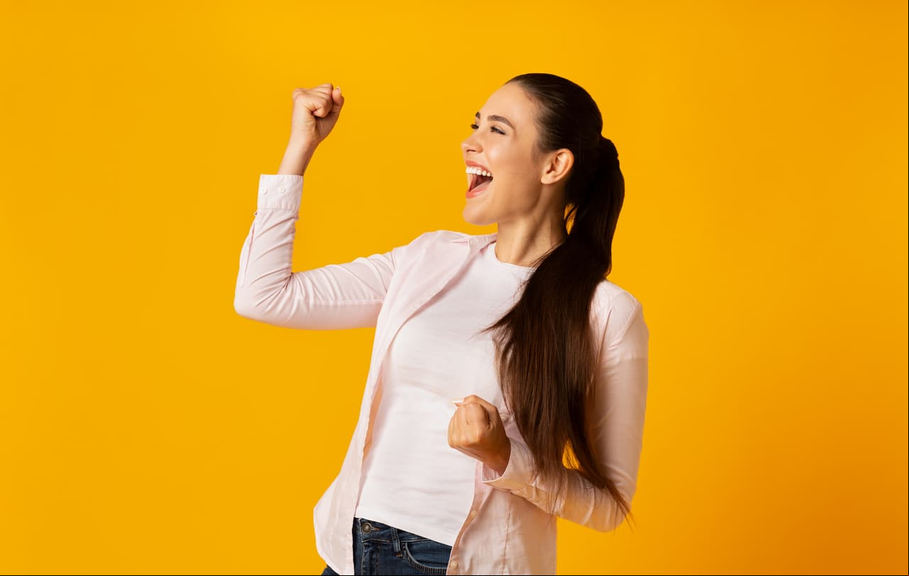 Rejoicing Success. Young Woman Shaking Fists Celebrating Victory On Yellow Background In Studio. Empty Space