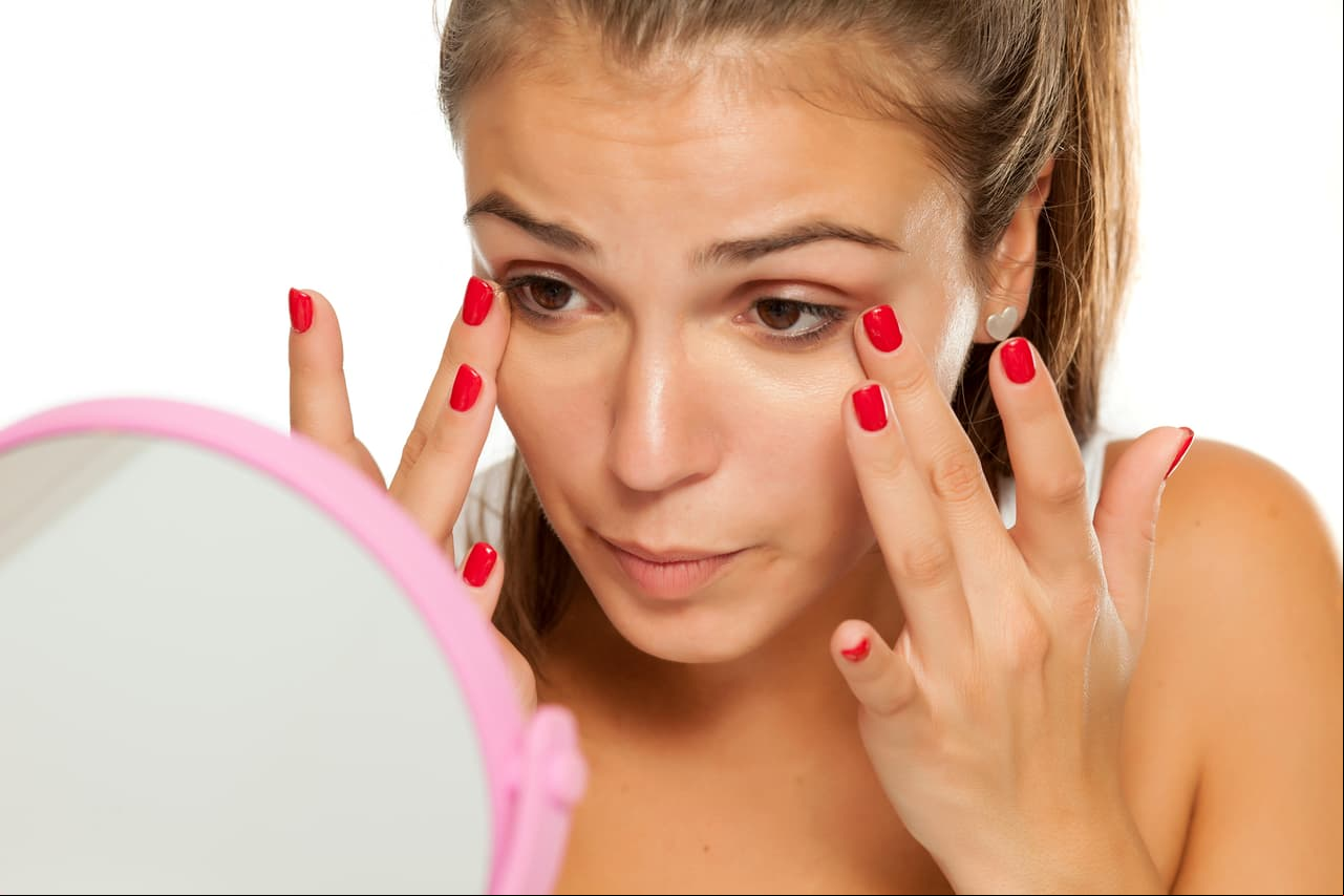 young women applied concealer under the eyes with her fingers