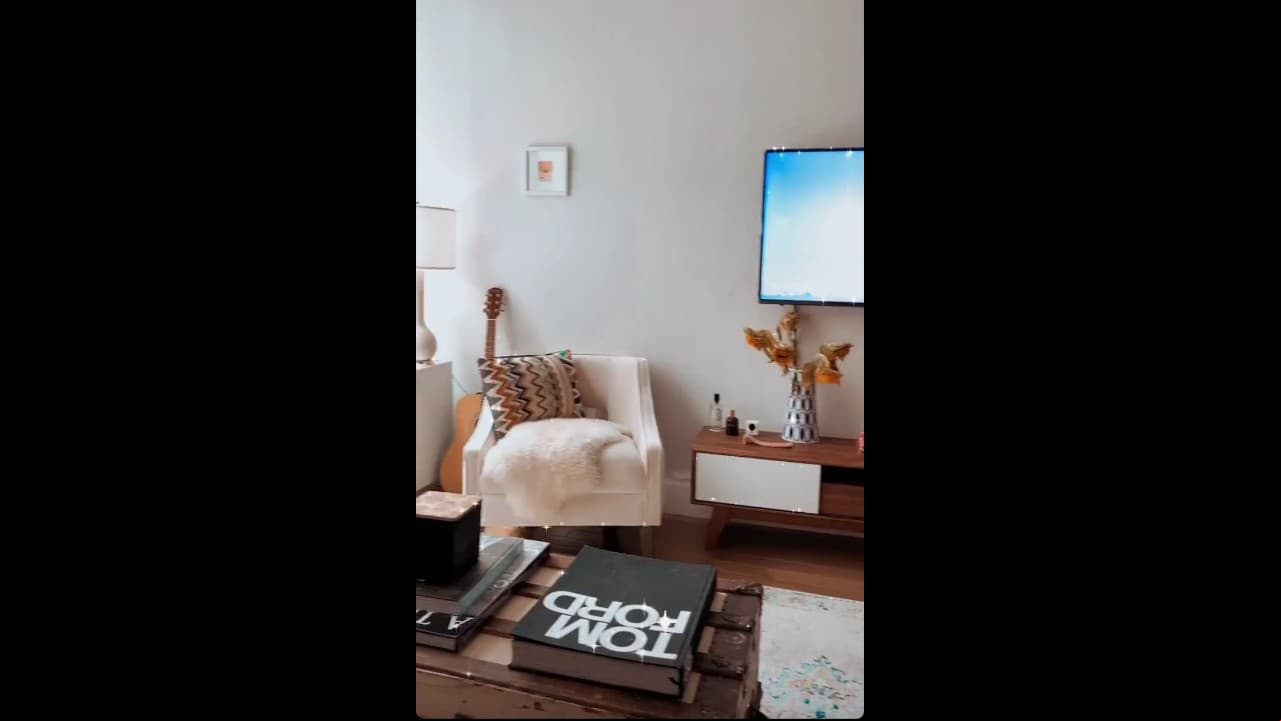 Frente a su sillón, que hace juego con la pared, está la televisión y otros muebles en tonos claros.