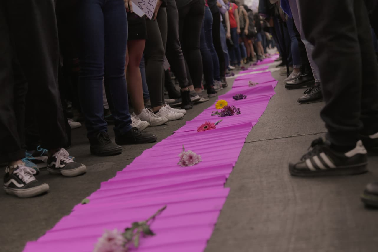 La manifestación comenzó dando un pase de lista con los nombres de víctimas de feminicidio, así como un homenaje que creó una gran cruz con flores y fotos de dichas mujeres fallecidas.