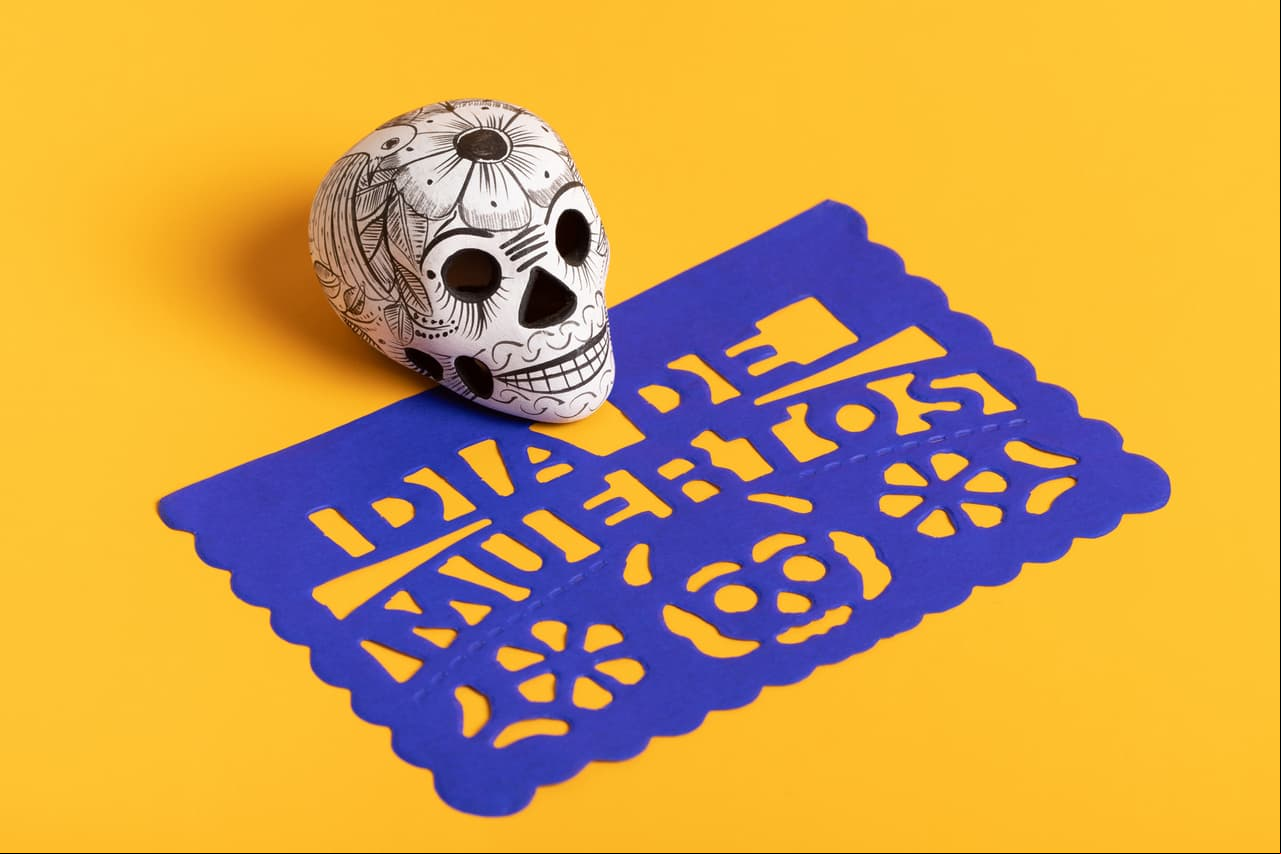 Day of the dead pottery skull (calavera) on blue papel picado on yellow background, Dia de Muertos background